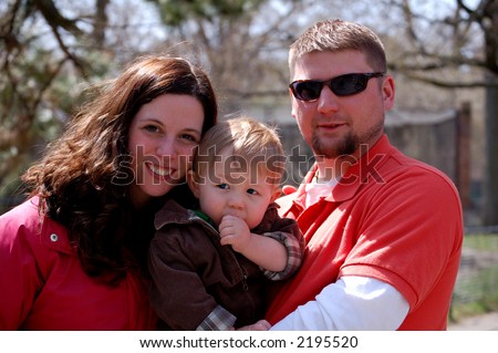 Young woman and young man holding a one year old boy who is sucking his thumb.