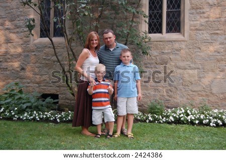 Young family of four standing in front of a church on a summer day. Boys are approximately five and seven years old.
