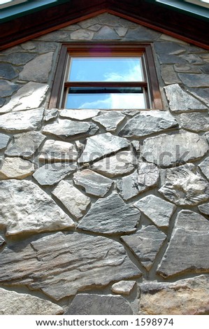 Looking up rock wall at window with sky reflection.