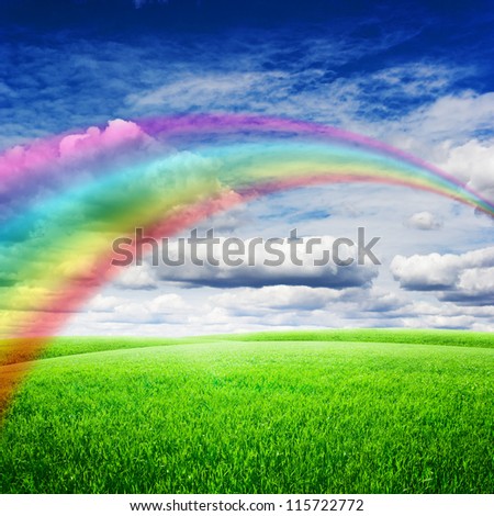 Green field under blue clouds sky with bright rainbow. Beauty nature background
