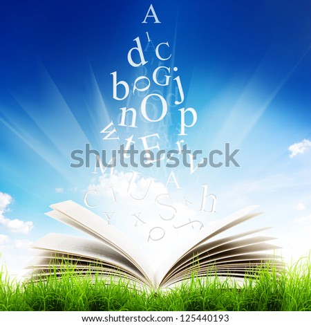 Open book with flying letters in green grass over blue sky background. Magic book