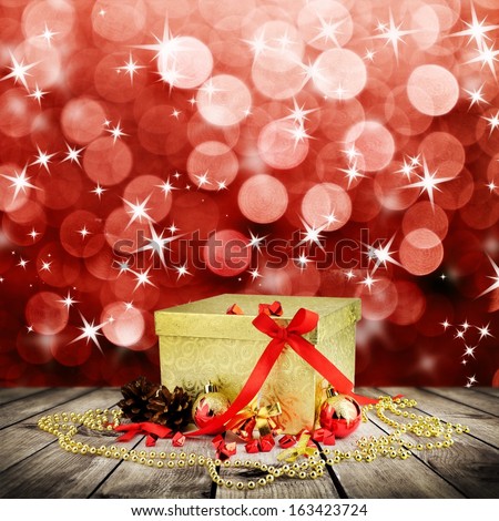 Golden christmas gift box with christmas balls on wooden planks over red blured background