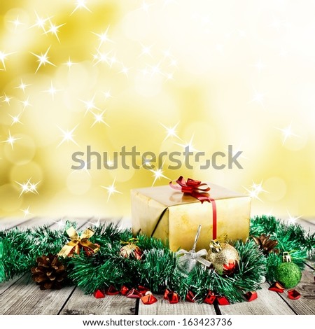 Golden christmas gift box with christmas balls on wood planks over abstract blur yellow background