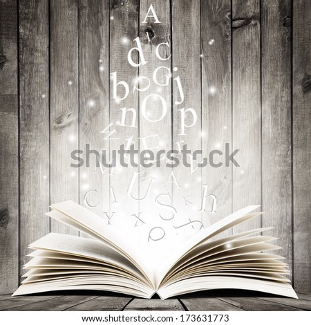 Open book with flying letters over wooden background. Magic book
