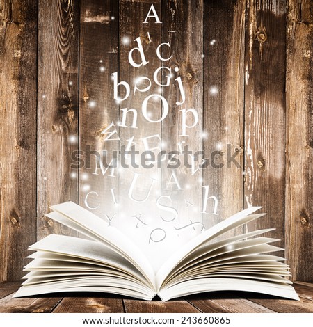 Open book with flying letters over wooden background. Magic book