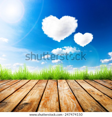 Green grass on wooden plank over a blue sky with hearts shape clouds. Beauty natural background