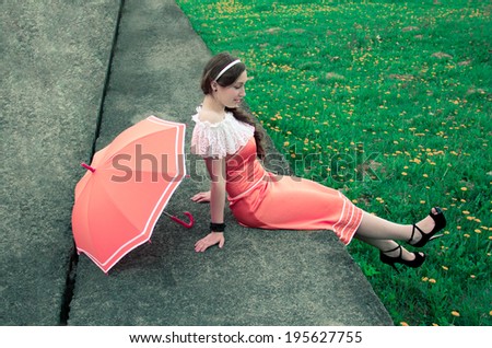 joyful girl with umbrella sits on a concrete slab on a background of green grass with Dandelion