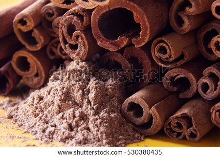 heap of cinnamon sticks close up and cinnamon powder on a yellow background