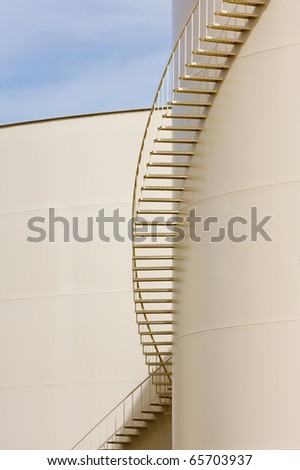 Shadows of the stairs as they curve around the side of this beige oil storage tank.
