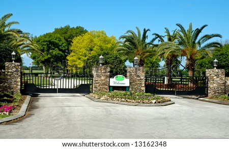 Rustic stone entrance with two electronic iron security gates and welcome sign and stone pillars with rustic lanterns on top.