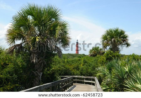 Ponce Lighthouse with lush, green foliage as seen from the hiking path and boardwalk at New Smyrna Beach, Florida.