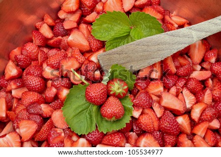 whole strawberries placed on strawberries leaves among sliced strawberries for jam