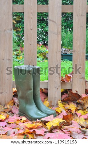 rubber boots on leaves in front of a wooden fence in the garden