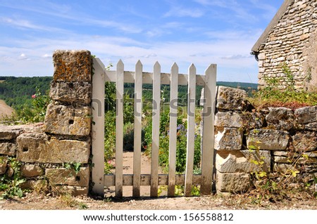 small white gate between stones in a low wall overlooking a country garden