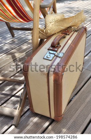 straw hat on small retro suitcase next to a lounge chair on wooden terrace