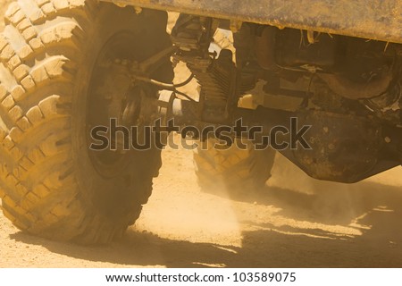 Detailed view of the wheels, tires and truck shaft that goes in the dust of the desert. The rays of light shine through the wheels.