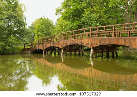 Wooden bridge over a quiet river, lined with green trees (Lednice, Czech Republic)