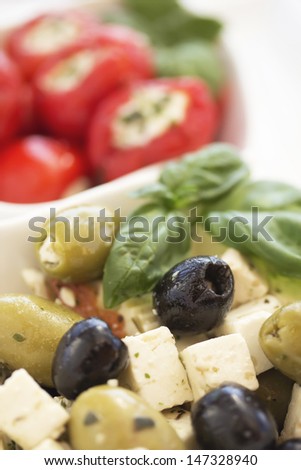 Salad of black, green olives with pieces of cheese. Garnished with basil leaves. The white bowl. Spicy round red peppers stuffed with cheese in the background.