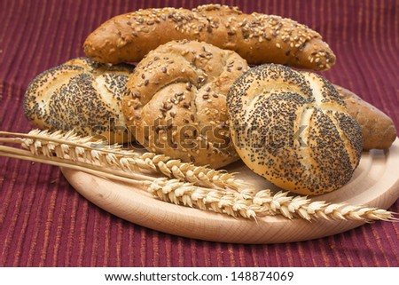 Various types of whole wheat bread and wheat ears lying on a wooden board.