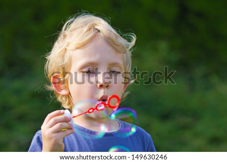 Blond boy making soap bubbles outside (green background)