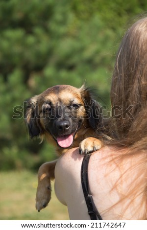 Young woman is holding a dog. Woman is turned back to the camera and the dog is looking over her shoulder at the camera. Shooting outdoors.