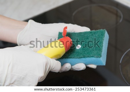 Cleaning of the kitchen hob. Woman is applying a cleaner to a sponge.