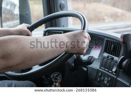 Closeup view from the truck cab. Truck driver keeps driving wheel with both hands.. Navigation is mounted on the vehicle dashboard.
