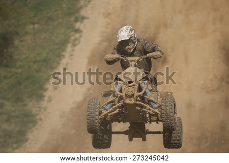 Front view of guad racer jumping. The quad bike and rider are very muddy.Potential trademarks are removed and face of the racer is unidentifiable.