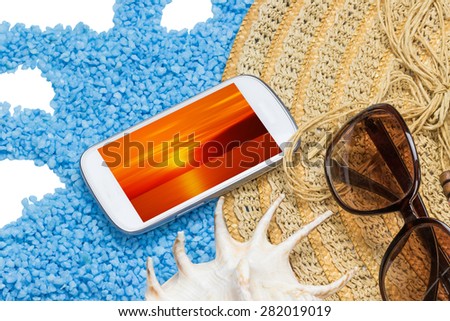 Straw hat, sunglasses and a seashell are lying on a little blue stones isolated on the white. Display of the white cell phone contains photo of blurred sunset. All potential trademarks are removed.
