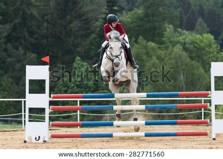 SVEBOHOV, CZECH REPUBLIC - MAY 23: Front view of young  horsewoman in red jacket on white horse, that is jumping at \