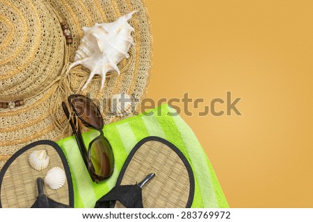 Straw hat, sunglasses, beach sandals, green towel  and seashells are on the left side of the photo. All is on the yellow background with sand texture. All potential trademarks are removed.
