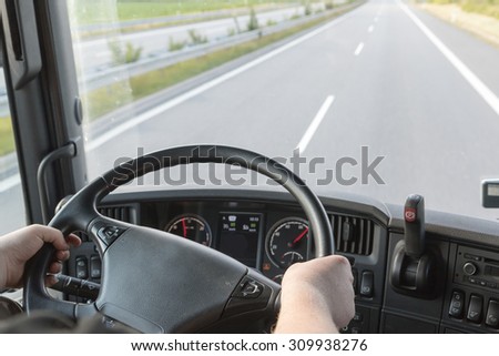 The driver is holding the steering wheel and is driving a truck on the empty highway. Focused on the wheel and drivers hand.