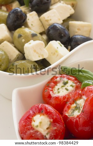 Spicy round red peppers stuffed with cheese, garnished with basil. The white bowl. Salad of olive and cheese in the background.