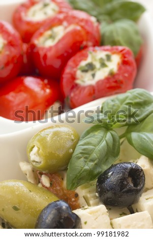 Salad of black, green olives with pieces of cheese. Garnished with basil leaves. The white bowl. Spicy round red peppers stuffed with cheese in the background.