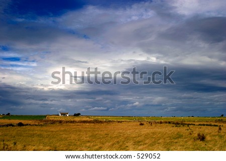 Small house in the distance of a wide open flat landscape with approaching storm