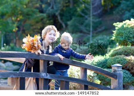 happy smiling mother and her cute son at fall time, family of two with yellow autumn leaves