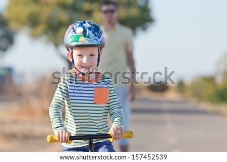 smiling happy little boy at the balance bike and his young father in the background