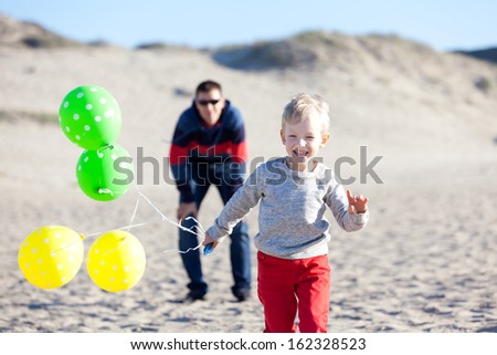 little excited boy running away from his parent with colorful balloons