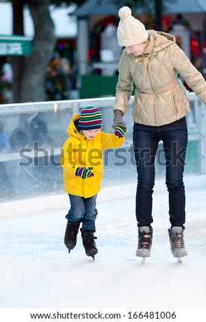 happy smiling mother and her cute cheerful son ice skating together at winter