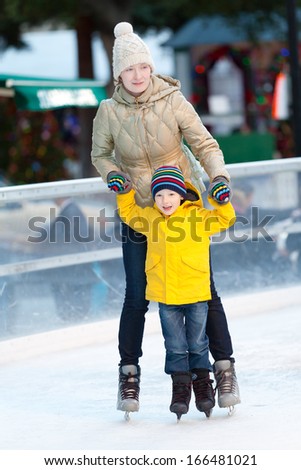 happy smiling mother and her cute cheerful son ice skating together at winter