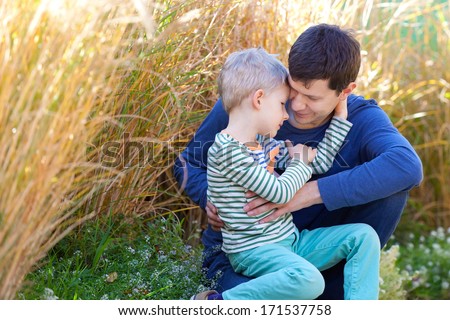 happy family of father and son sitting outside and hugging