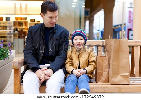 family of young father and excited son sitting on the bench in shopping mall