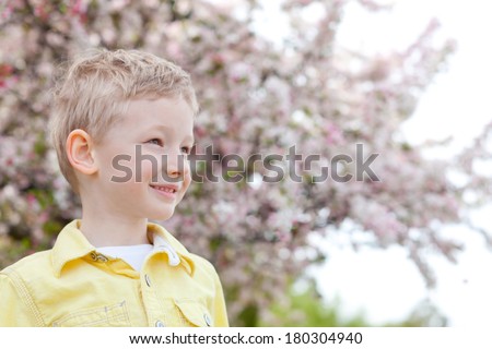 cheerful smiling boy looking forward with beautiful blooming apple tree in the background at spring time