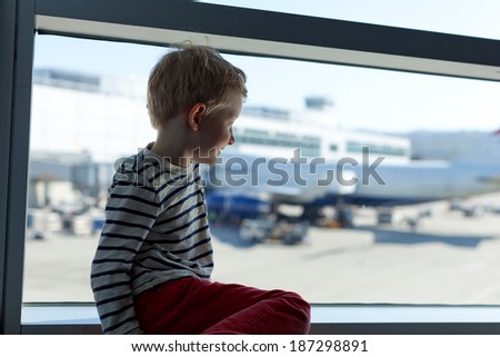 smiling little boy waiting at the airport and looking at the big plane through the window