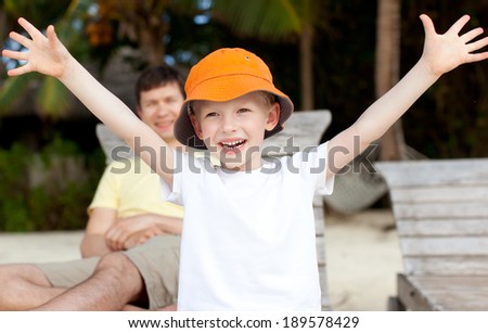 cheerful little boy with his hands up and his smiling father at the background, vacation together