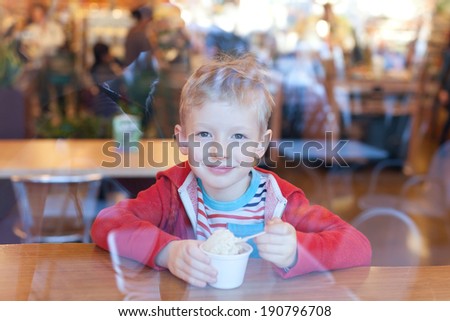 positive smiling little boy eating ice-cream at cafe, view through the window