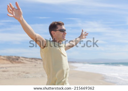 young smiling man standing at the beach with arms wide open, freedom or happiness concept