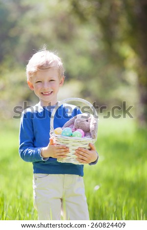 little smiling boy holding basket with easter eggs and bunny after egg hunt in the park