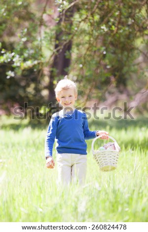 little smiling boy holding basket with easter eggs and bunny after egg hunt in the park