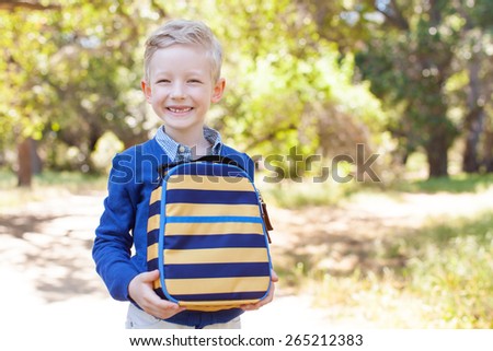 smiling little schoolboy holding lunchbag ready to go to school, back to school concept